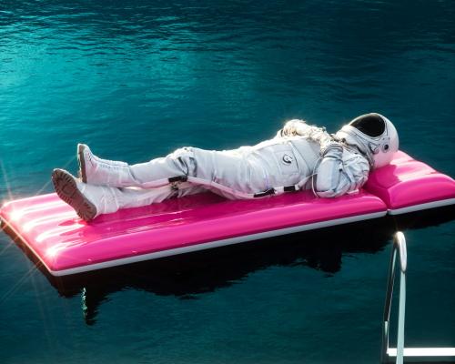 Astronaut, der entspannt auf einer pinken Luftmatratze im Wasser liegt